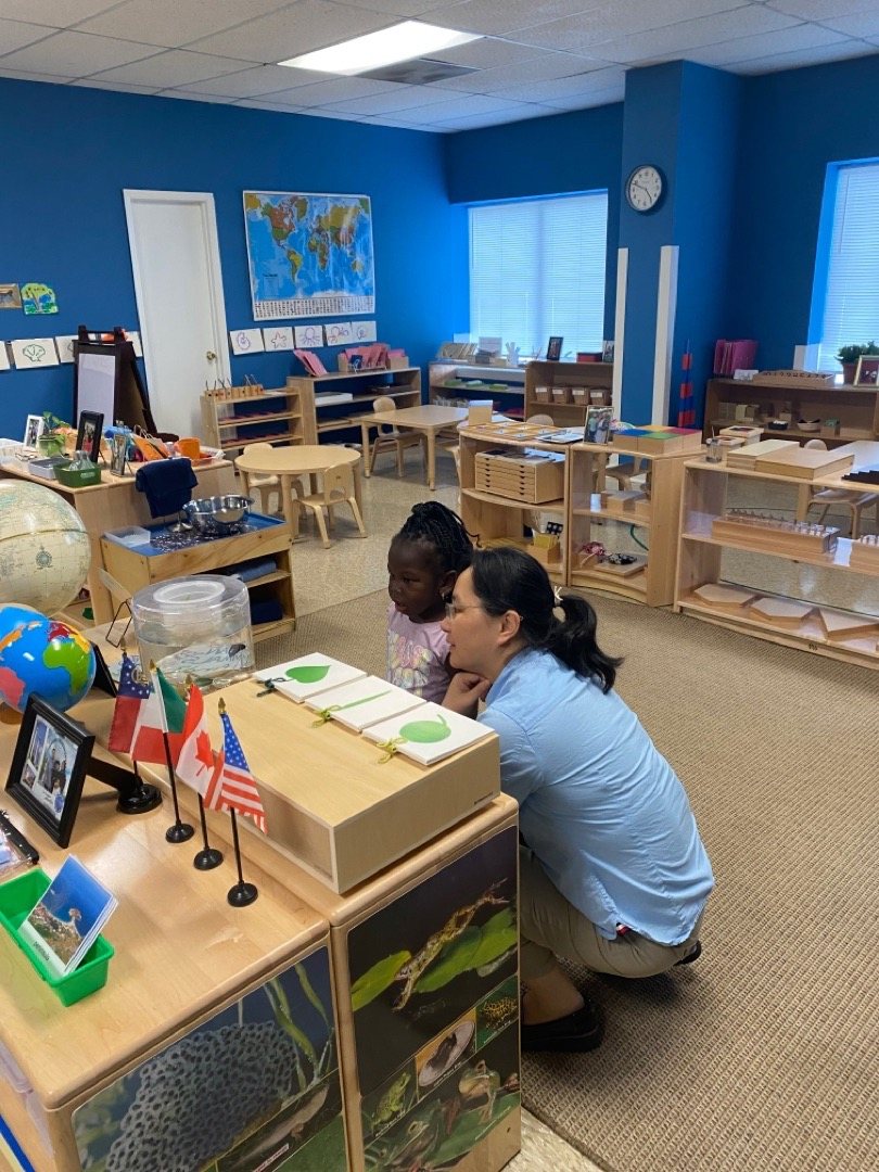 A Seven Oaks teacher works with a student at the geography shelf with flags and globes