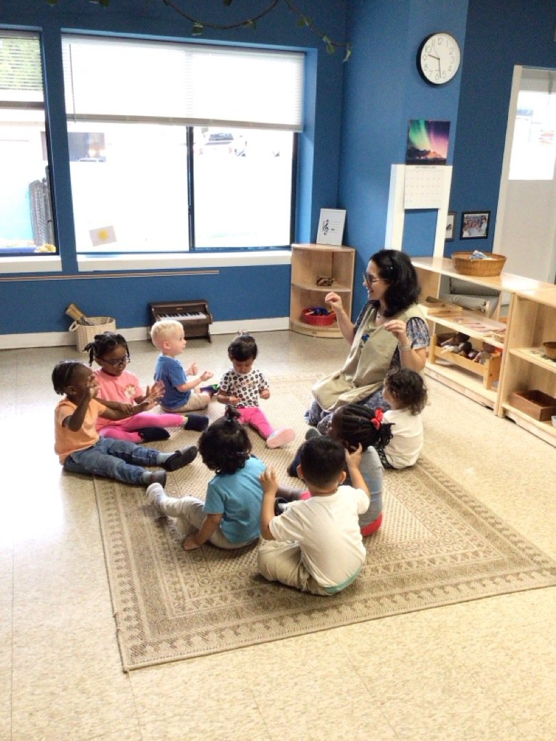 Primary students sit in a circle on the rug with their teacher