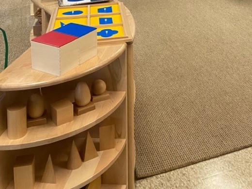 Montessori sensorial materials on a classroom shelf: the binomial cube, geometric solids and metal insets