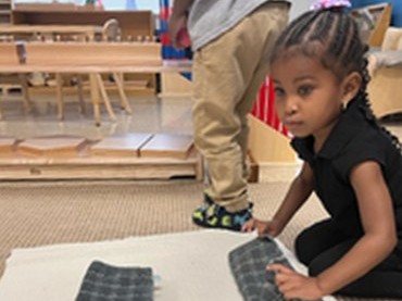 A Seven Oaks student folds cloths on a work rug during a Practical Life lesson