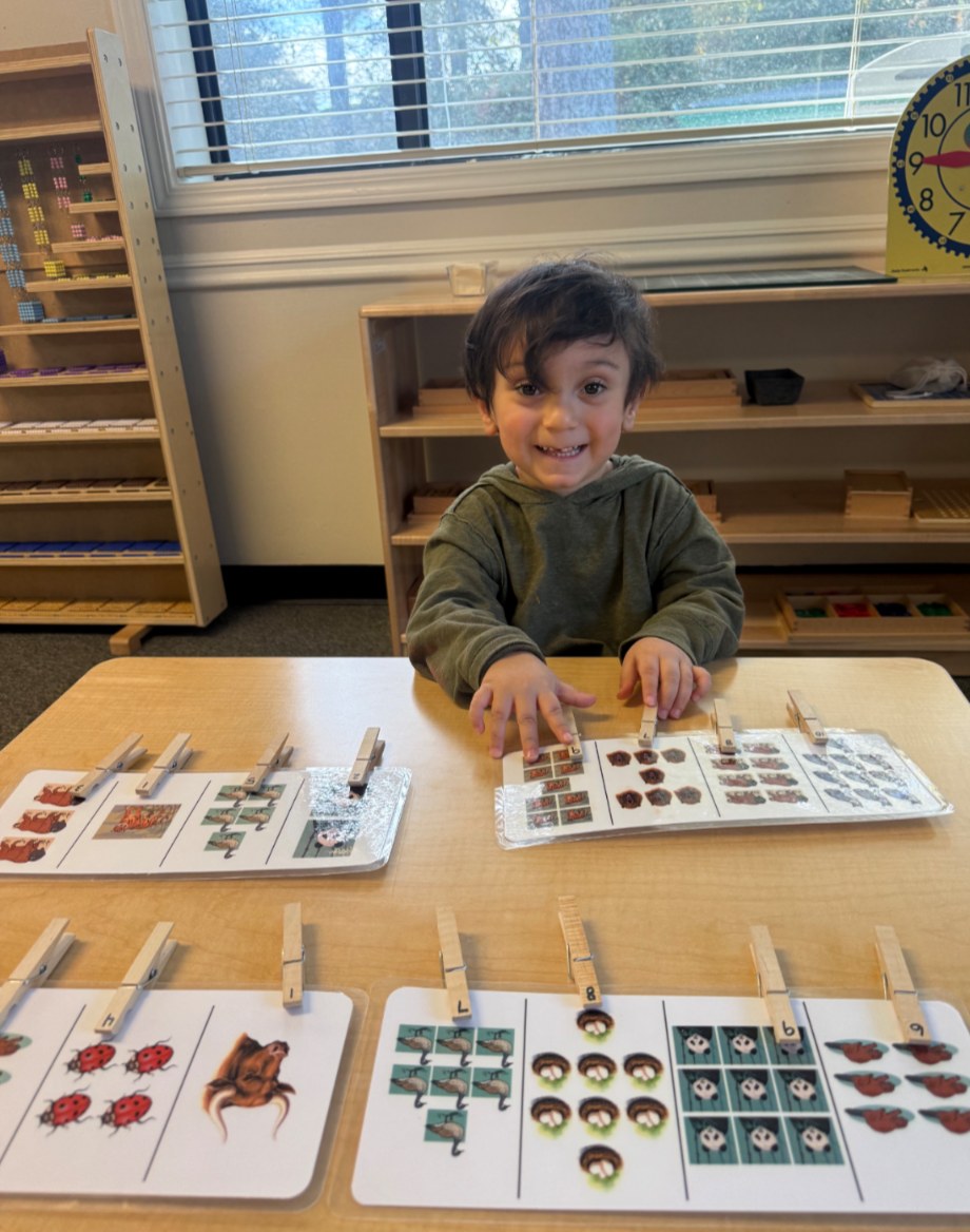 A smiling Seven Oaks Primary student works on clothespin counting cards at a classroom table